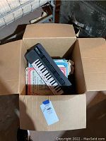 Yamaha electronic keyboard with labeled keys and music books inside cardboard box.
