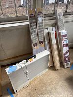 Photo of multiple new window blinds in original packaging standing next to an unwrapped window blind and a SunRay light box placed on the floor near a window.