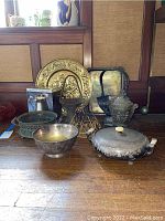 Tabletop display of various metal bowls, baskets, decorative plates, lidded containers, and a boxed Royal Limited pitcher.