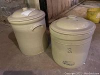 Two beige stoneware crocks with lids placed on the floor showing overall condition and size.