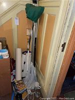 Photo showing multiple curling brooms with wooden handles and green cover bag, books and glassware at base