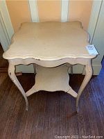 Front view of scalloped edge end table showing top surface and curved legs with visible wear and nicks.