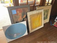 Group of five art pieces arranged on floor including framed and unframed items, showing variety and condition.
