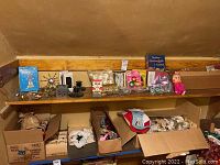 Photo showing shelf with assorted Christmas ornaments, candle holders, Santa clock, Herman Pecker doll, and boxes with other holiday décor items.