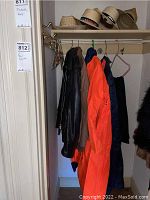 Four hats displayed on a shelf, leather jacket, rain jackets, and pants hanging on rack