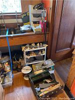 Overview of jewelry making area showing plastic storage bin, metal dome rack, toolbox and hand tools on floor
