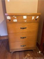 Frontal view of wood dresser showing four drawers with metal handles and sticker residue on top drawer.