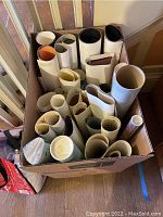 Top view of a cardboard box filled with multiple rolled posters of various sizes and colors.