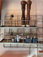 Metal wall racks mounted on wall, holding pepper mills and salt shakers