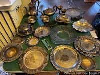 Wide view of the entire silver plate serving pieces set laid out on a green cloth, showing teapot, sugar bowl, creamer, trays, covered dishes, and various serving pieces