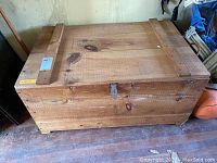 Front view of solid wood trunk featuring two wooden slats on top and a metal latch in the center.
