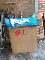 Cardboard box containing vibratory tumbler parts wrapped in blue packing material under garage setting