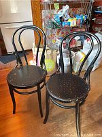 Two black painted bentwood side chairs placed on wooden floor with some chipping and paint wear visible on seats and backs.