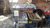 Wide view of NHL Stanley Cup table hockey game with vintage board games stacked on a table in a garage setting.