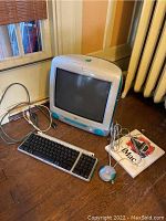 Front view of the vintage Apple iMac M5521 with keyboard, mouse, and iMac manual on wooden floor next to radiator and window.