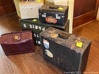 Group photo displaying four vintage luggage pieces: large black suitcase with initials and stickers, smaller black suitcase with Cunard Line sticker, white cosmetic case, and brown leather bag with visible wear.