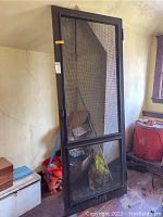 Full view of vintage screen door standing upright showing wood frame and metal screen