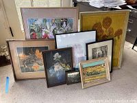 Eight framed artworks displayed on the floor, showing variety of floral and landscape paintings including one sunflower Van Gogh poster