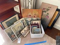 Multiple framed artworks and prints grouped on floor and inside box, showing size and variety