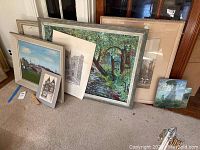 Group of seven framed and unframed wall art pieces arranged leaning against a wall