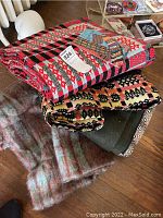 Four blankets stacked: red/black/gray geometric; yellow/black; olive green; mottled brown/teal striped