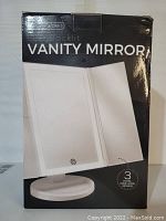Front of the box showing the product name, 'Vanity Mirror' with 3 panel wide-angle view illustration, circular base, and touch sensor symbol.