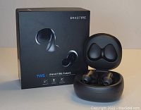Photo showing a pair of black EnacFire Future earbuds alongside their charging case and original black box packaging. The earbuds are placed inside the open charging case revealing the internal mold for the earbuds.