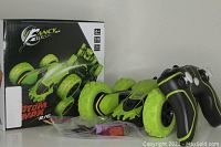 Green Fancy Stunt Atom Max RC 3 King remote control car with green wheels and black/green remote controller shown alongside original box and accessories in plastic bag.