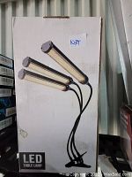 Box of the LED table lamp showing the image of the lamp with three adjustable light bars and a clamp base.