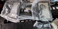 Photo showing two rectangular LED panel lights with diffusers, each sealed in plastic bags, along with two metal tripods, power cords, and remote controls all sealed inside packaging.