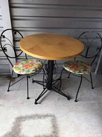 Front view of round wood top bistro table with two black metal chairs featuring floral seat cushions
