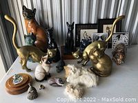 Wide view of all cat figurines and framed art prints on a table showing variety and condition