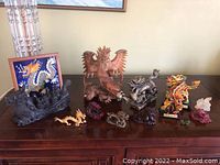 Wide view of various dragon figurines on a wooden surface including a framed dragon tile artwork, large brown wooden dragon, colorful and black dragons