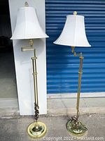 Two brass floor lamps with white shades shown side by side against blue storage door, cords wrapped at base, adjustable arms visible.
