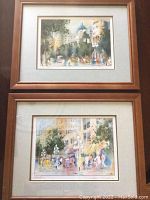Two framed watercolor prints showing city street scenes with muted colors and people, both approx. 8x10 inches with light wooden frames and visible mat surrounding prints.