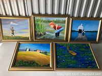 Five framed paintings displayed against a corrugated metal wall, showing a range of outdoor scenes with children, nature, and countryside.