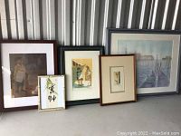 Five framed artworks arranged on floor leaning against wall, showing size and framing style