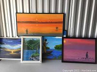 Group photo of 5 framed artworks showing variety of landscapes including sunset scenes, figures, water, and mountains, some frames show scratches.