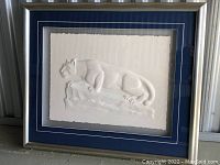 Framed white relief art piece showing a panther lying on a rock, with blue matting and a scratched frame.