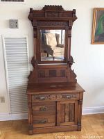 Front view of the antique wooden hall stand showing its rectangular mirror, carved details on top, and base with drawers and cabinet door.