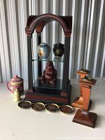 Wooden arched display stand with various decorative ceramic items on glass shelves and wooden candle holders arranged beside it.
