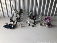 Overview photo showing entire collection of various dragon figurines made from metal, glass, and crystal, displayed on a white surface.