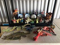 Photo showing variety of dragon and mythical creature figurines including wooden puppets and ceramic pieces along with decorative plates on display shelf and floor