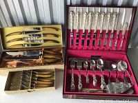 Full view of mixed flatware sets including ornately detailed and faux tortoiseshell handle pieces in display boxes