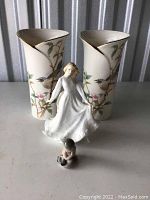 Front view of two bird and floral porcelain vases with gold trim and two figurines in front, a dancing woman and a seated child