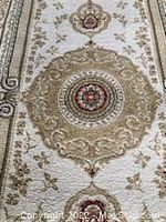 Close-up of curved medallion design in center pattern of the rug in beige, brown, and red colors on a pale cream background with floral detailing.