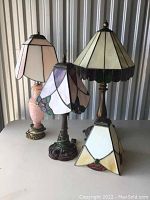 Four stained glass table lamps displayed on a flat surface, showing different styles and colors of stained glass shades and bases.