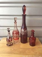 Photo of all four vintage red glass decanters arranged side by side on wood surface against a neutral backdrop.