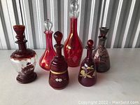 Front view of six ruby red vintage glass decanters with stoppers, standing aligned showing variation in size and decoration