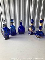 Overall shot of the five vintage cobalt blue glass decanters with gold floral and ornamental detailing arranged in a row